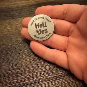 May include: A silver coin with the text "What's it going to be?" and "Hell Yes" in a bold font. The coin also has the text "Decision Coin" on it.