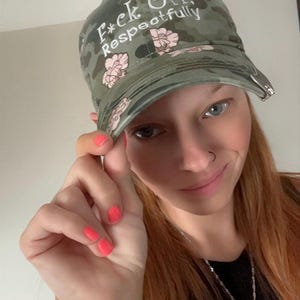 Op de afbeelding: Camouflage baseballpet met de tekst "F*ck Off, Respectfully" in witte letters. De pet heeft roze bloemenaccenten. De hoed is een casual accessoire.