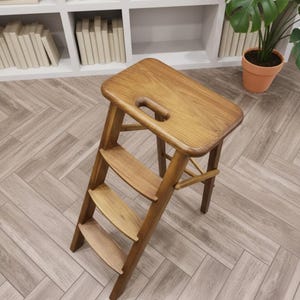 May include: A wooden step stool with three steps and a rectangular top with a handle cutout. The stool is made of light brown wood and is angled towards the viewer. The background includes a bookshelf and a potted plant.