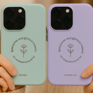 May include: Two phone cases, one mint green and one lavender, are displayed. Each case features a floral design and the text "Bold power and glorious majesty are wrapped around her" with the word "Proverbs" printed below.