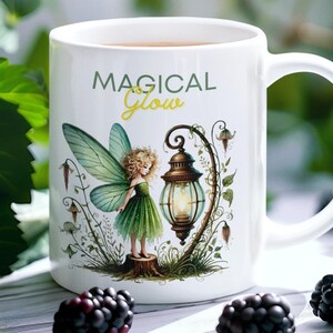 May include: White ceramic mug with a green fairy illustration and the text "MAGICAL Glow" in green and gold lettering. The fairy is standing next to a glowing lantern.