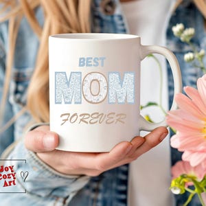 Puede incluir: Taza de cerámica blanca con un diseño de purpurina azul y blanca que dice "Best Mom Forever".