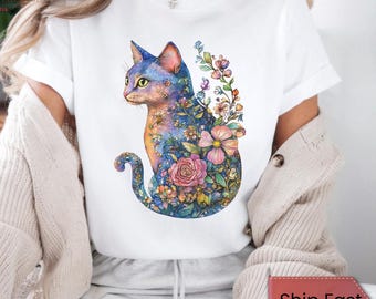 May include: White t-shirt with a colorful illustration of a cat with flowers. The cat is sitting with its tail curled around its body. The flowers are in shades of pink, blue, and purple.