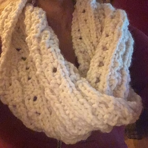 May include: A white crocheted infinity scarf with a textured pattern.
