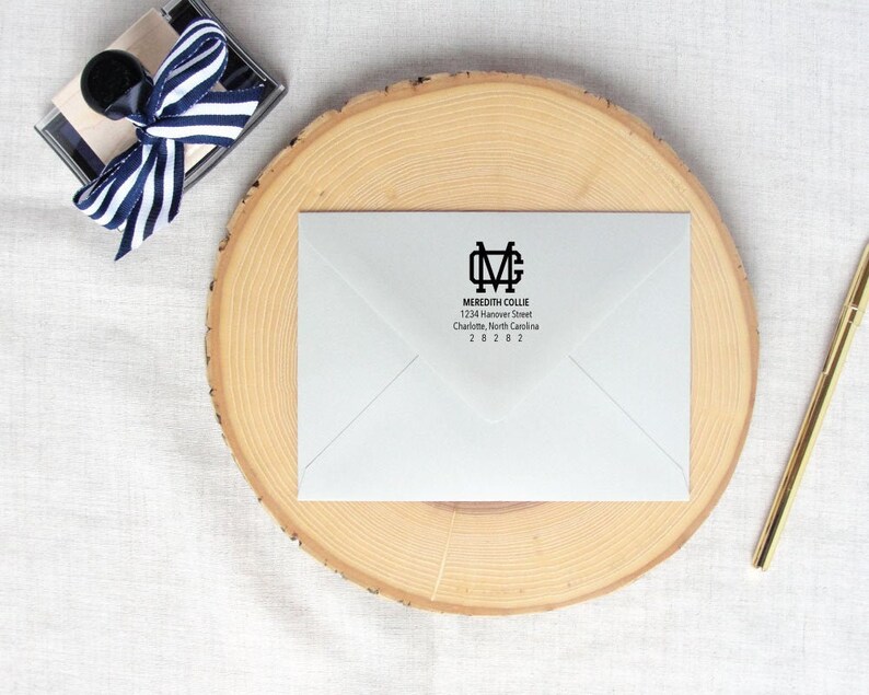 Op de afbeelding: Een witte envelop met een zwart retouradreslabel. Het label heeft een monogram met de initialen "MC" in een vetgedrukt, bloklettertype. De tekst "Meredith Collie" staat onder het monogram, gevolgd door het adres "1234 Hanover Street, Charlotte, North Carolina 28282".