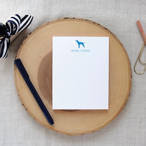 May include: A white notepad with a blue dog silhouette and the text "MICHAEL P. BOSTIAN" printed on the top. The notepad is on a wooden surface.