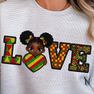 Può includere: Una felpa bianca con la scritta "LOVE" in un design colorato. La "L" è verde, gialla e rossa. La "O" è una ragazza dei cartoni animati che tiene un cuore. La "V" è rossa, verde e gialla. La "E" è un disegno a fantasia.