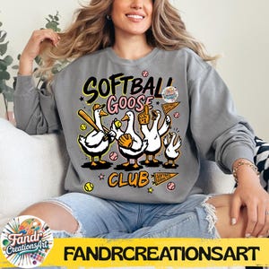 May include: Gray sweatshirt with a graphic of cartoon geese playing softball. The text "Softball Goose Club" is above the geese. The geese are wearing baseball caps, gloves, and holding bats and flags. The sweatshirt has long sleeves.