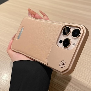 May include: A blush-colored phone case with a textured leather-like finish. The case features a camera cutout with three lenses and a speaker. A silver-colored accent is on the side of the case.