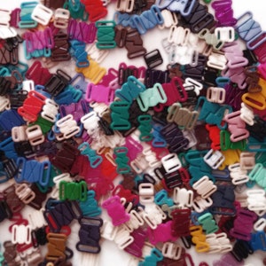 Könnte beinhalten: Ein großer Haufen bunter Plastik-BH-Gurtversteller. Die Versteller sind in verschiedenen Farben, darunter Rot, Blau, Grün, Lila und Weiß.