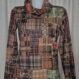 May include: A long-sleeve top featuring a cowl neckline and a multi-coloured patchwork pattern. The design consists of various rectangular blocks in shades of orange, brown, black, and green, displaying diverse textures and plaid-like motifs.