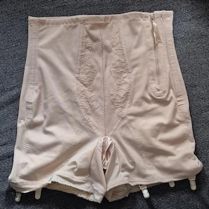 May include: A high-waisted beige shapewear garment featuring a side zipper closure, vertical lace panels on the front, and multiple garter clips attached to the bottom hem. The fabric is smooth and opaque with reinforced stitching throughout the design.