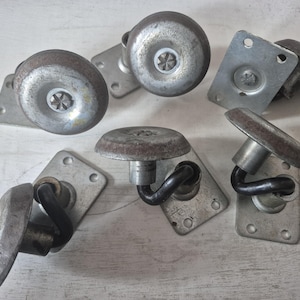May include: A collection of six industrial-style metal casters featuring circular silver-toned wheels with central star-shaped screws. Each caster includes a rectangular mounting plate with pre-drilled holes and a curved black metal support arm.