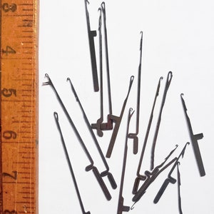 Könnte beinhalten: Eine Gruppe von 14 silbernen Metall-Fadenziehern, auch bekannt als Garnnadeln, liegen auf einer weißen Oberfläche verstreut. Die Nadeln werden zum Einfädeln von Garn durch kleine Löcher verwendet.