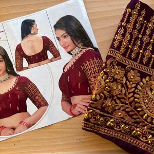 Puede incluir: Una blusa de terciopelo granate con bordados y adornos dorados. La blusa tiene un escote en V profundo y mangas tres cuartos. La tela es ricamente texturizada y el bordado es intrincado. La blusa es una prenda tradicional india.