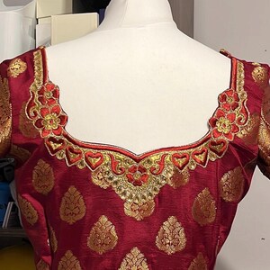 May include: A red and gold embroidered blouse with a decorative neckline. The blouse features a floral pattern and is made from a luxurious fabric.