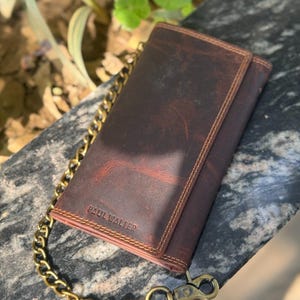 May include: A brown leather wallet with a gold chain attached. The wallet has a distressed finish and the text "PAUL WALTER" is visible. The chain is thick and has a clasp.
