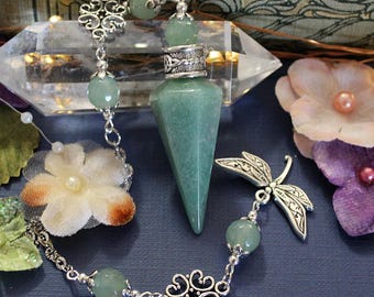 May include: A green stone pendulum with a silver-toned metal cap featuring intricate knotwork. The chain includes green stone beads, a silver-toned dragonfly charm, and a decorative floral link. A black label displays WhiteRaven's Designs.