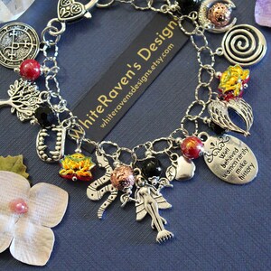 May include: A silver-toned charm bracelet featuring various pendants including a tree, a snake, a fairy, vampire fangs, and an oval tag with the text 'Well behaved women rarely make history'. The bracelet includes red, black, and metallic beads.