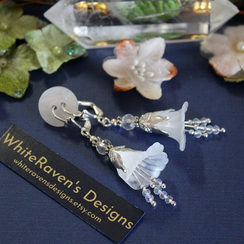 May include: White flower earrings with crystal accents. The earrings are silver-toned and feature a delicate flower design with a crystal drop.