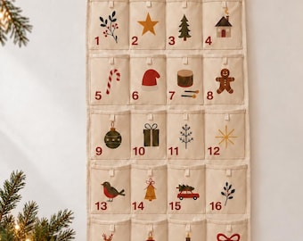 Könnte beinhalten: Ein cremefarbener Adventskalender aus Stoff mit spitzem Abschluss, personalisiert mit dem Namen Charlotte in roter Schrift. Er verfügt über vierundzwanzig nummerierte Taschen, die jeweils mit einem weihnachtlichen Motiv in Rot, Grün und Gold verziert sind.
