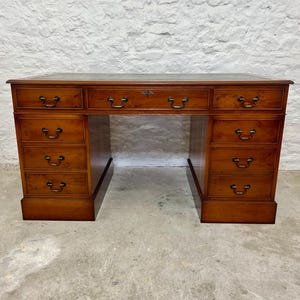 May include: A wooden desk with a dark brown top and a light brown body. The desk has multiple drawers with brass handles and a keyhole in the centre. A classic piece of furniture.