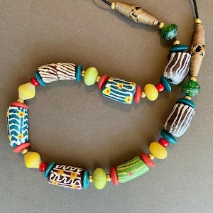 May include: A colorful necklace with green, yellow, red, and white beads. The beads are cylindrical and have different patterns. The necklace is made of wood and has a gold clasp.