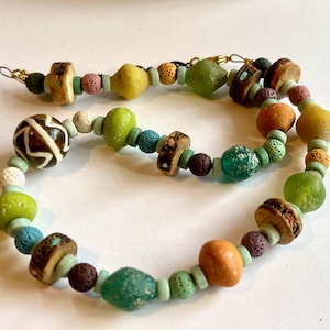 Peut inclure: Un collier de perles coloré avec des perles vertes, brunes, orange, blanches et bleues. Le collier présente une variété de textures, notamment des perles lisses, rugueuses et texturées.