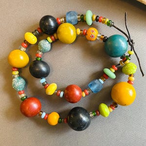 May include: A handcrafted necklace featuring a variety of colorful beads. The necklace includes large, round beads in yellow, red, and black, interspersed with smaller, multi-colored beads. The necklace is approximately 18 inches long.