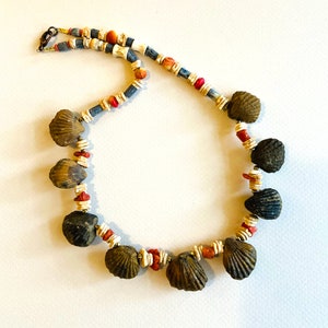 May include: A necklace made of small seashells, red and white beads, and blue and white cylindrical beads.