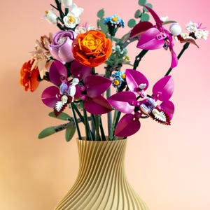 May include: A vibrant bouquet of colorful flowers in a gold vase. The arrangement includes orange, purple, and white blooms, with green stems and leaves. The vase has a textured, swirling design.