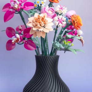 May include: A black vase with a swirling design holds a vibrant bouquet of colorful flowers. The flowers include pink, orange, and white blooms, with green stems. The arrangement is set against a gradient purple background.