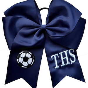 May include: Navy blue cheer bow with a white soccer ball and the letters "THS" embroidered in white.