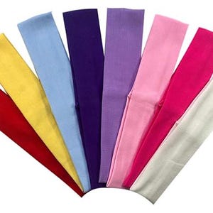 Peut inclure: Une collection de bandeaux colorés disposés en éventail. Les bandeaux sont de différentes couleurs unies : rouge, jaune, bleu clair, violet, lavande, rose, rose vif et blanc. Les bandeaux sont faits d'une matière souple.