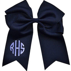 May include: Navy blue cheerleading bow with a monogram in light blue. The bow is made of a grosgrain ribbon and features a large, classic bow shape with long tails. The monogram includes the letters RHS.