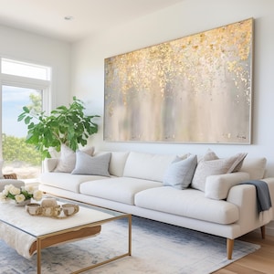 Könnte beinhalten: Ein weißes Sofa mit Kissen steht vor einem großen abstrakten Gemälde in Gold- und Grautönen. Das Gemälde hängt an einer weißen Wand.