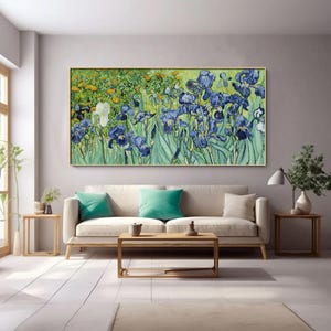 May include: A framed print of a floral painting featuring blue and white irises, with green foliage and yellow flowers in the background. The artwork is displayed above a beige sofa with teal cushions in a living room setting.