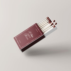 Pu&ograve; includere: Una scatola di fiammiferi bordeaux con la scritta "A Match Made in Heaven" in elegante corsivo. La scatola &egrave; aperta, rivelando fiammiferi bianchi con punte marroni. Il design &egrave; semplice e sofisticato.