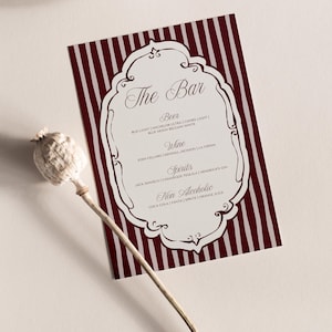 Puede incluir: Una tarjeta de menú de bar a rayas burdeos y blancas con un borde adornado. El texto "The Bar" está en la parte superior, seguido de categorías de bebidas: Cerveza, Vino, Licores y Sin alcohol. Una cabeza de semilla de amapola seca está en primer plano.