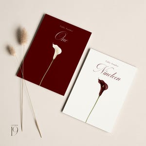 May include: Two wedding table number cards. One card is burgundy with a white calla lily and the word "One". The other card is white with a dark burgundy calla lily and the word "Nineteen".