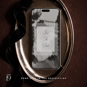 May include: A smartphone displaying a Save The Date announcement with a white lace-style border on a black and white background. The phone rests on an oval silver tray accompanied by a black velvet ribbon. Text includes October 19 and Demo Link.