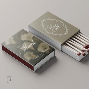 May include: Two rectangular matchboxes with sliding trays. One box features a dark floral print with the text THE PERFECT MATCH, Camilla & Matthew, and OCTOBER 19, 2028. The other box is olive green with a white ornate frame and the monogram CM.