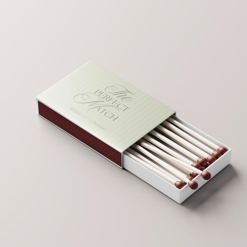 Puede incluir: Una caja de cerillas blanca con el texto "The Perfect Match" en escritura elegante. La caja est&aacute; abierta, revelando varias cerillas largas y blancas con puntas marrones. La tapa es de color verde claro.