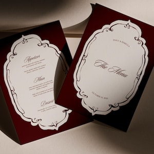 May include: Two burgundy wedding menu cards with decorative white frames. One card reads "The Menu" with the names "Emily & Rebecca" and the date "October 19, 2030." The other card lists an appetizer, main course, and dessert.