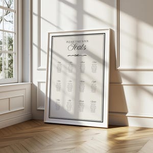 Może przedstawiać: Oprawiony na biało plan stołów z napisem "PLEASE TAKE YOUR Seats" w eleganckiej czcionce. Tabela podzielona jest na dwanaście sekcji, każda z listą nazwisk. Rama ma czarną obwódkę, na neutralnym tle.