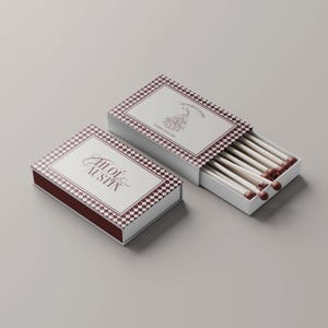 May include: Two matchboxes with a white and burgundy checkered design. One box is open, revealing several matches with brown tips. The text "All of Austin" is on one box, and "The Perfect Match" is on the other.