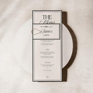 Może przedstawiać: Kremowa karta menu z czarnymi obramowaniami, z napisami "THE Menu" i "James Carter". Menu zawiera sałatkę z owocami morza, czarnego dorsza marynowanego w miso i sernik. Karta jest trzymana przez złoty spinacz.