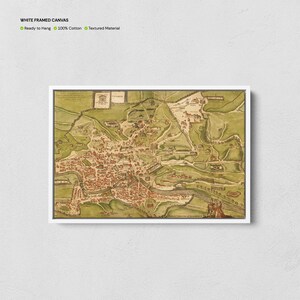 Op de afbeelding: Wit ingelijste canvas print met een gedetailleerde antieke kaart van een stad, met de nadruk op de stedelijke structuur en het omliggende landschap. De kaart is in bruine, groene en beige tinten. De tekst "WHITE FRAMED CANVAS" staat bovenaan.