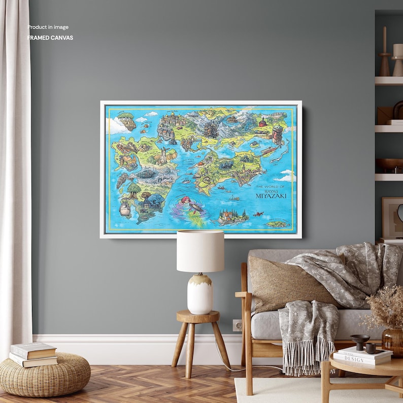 May include: A framed canvas print displaying a vibrant, illustrated map of the world of Hayao Miyazaki. The artwork, set in a white frame, hangs on a grey wall. The map features illustrations and the text "THE WORLD OF HAYAO MIYAZAKI".