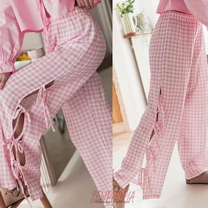K&ouml;nnte beinhalten: Rosa-wei&szlig; karierte Hose mit Seitenschlitzen und Bindeb&auml;ndern. Die Hose ist Teil eines passenden Sets, und der Stoff scheint leicht zu sein. Der Stil ist l&auml;ssig und bequem, geeignet f&uuml;r Loungewear oder Nachtw&auml;sche.